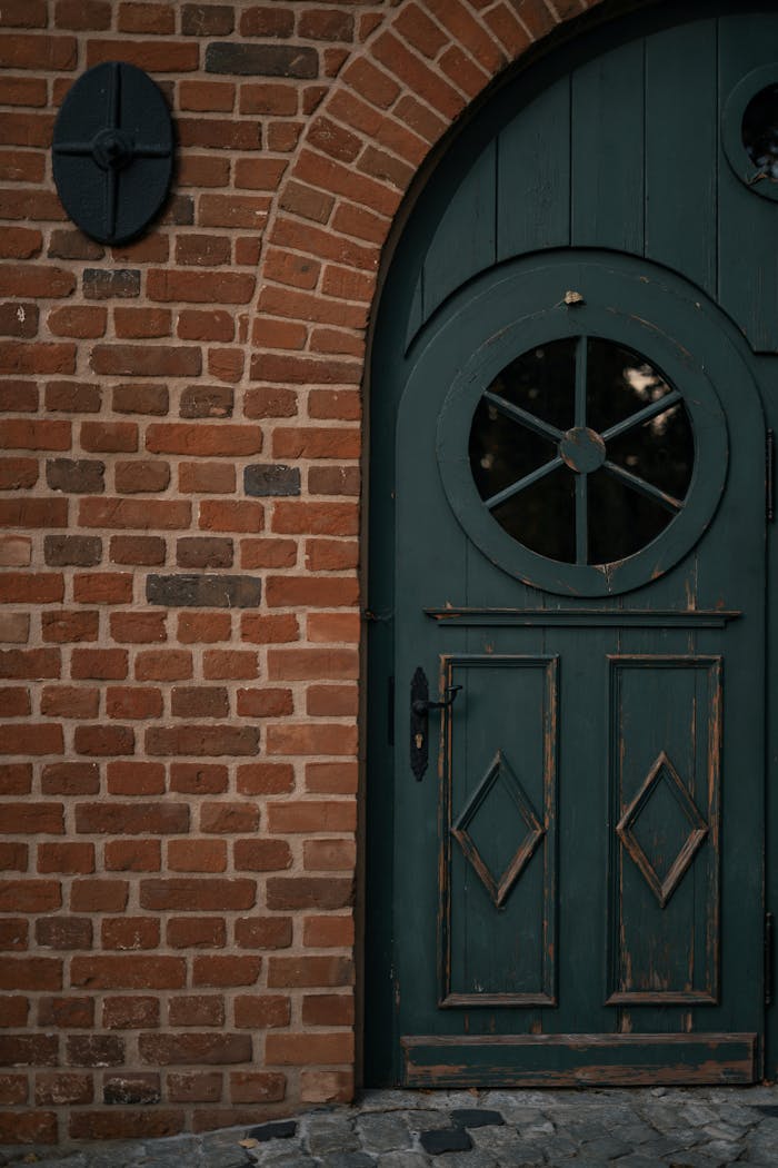 A rustic green wooden door set in an arched brick wall, showcasing vintage charm.
